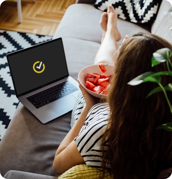소파에서 수박을 먹으면서 노트북에서 Norton 360 AntiVirus Plus를 실행하는 소녀.